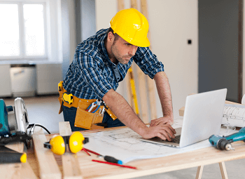 Contractor wearing a hardhat working on a laptop on a work table